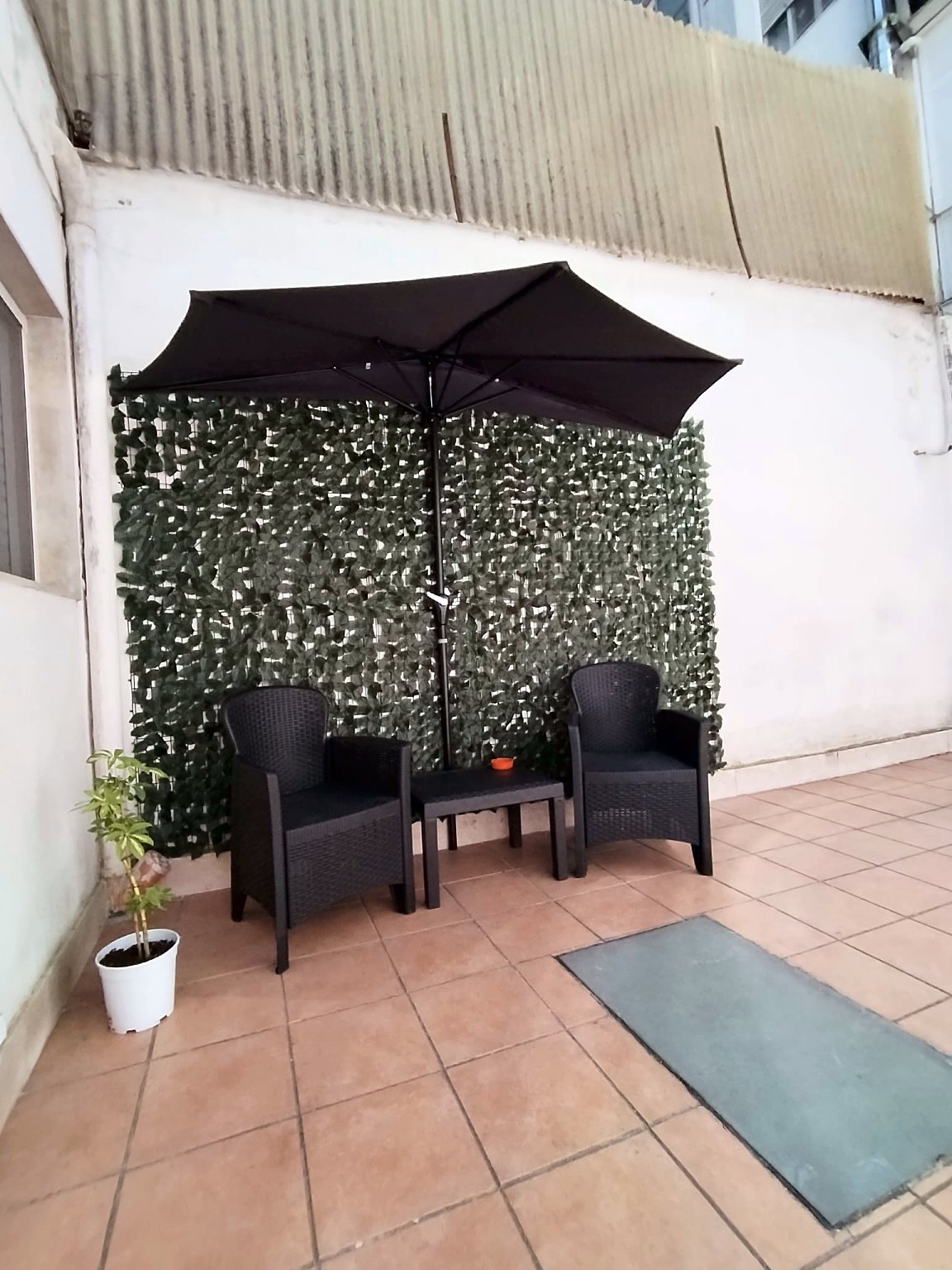 Cortile privato con ombrellone, due poltroncine e un tavolino davanti a una parete verde