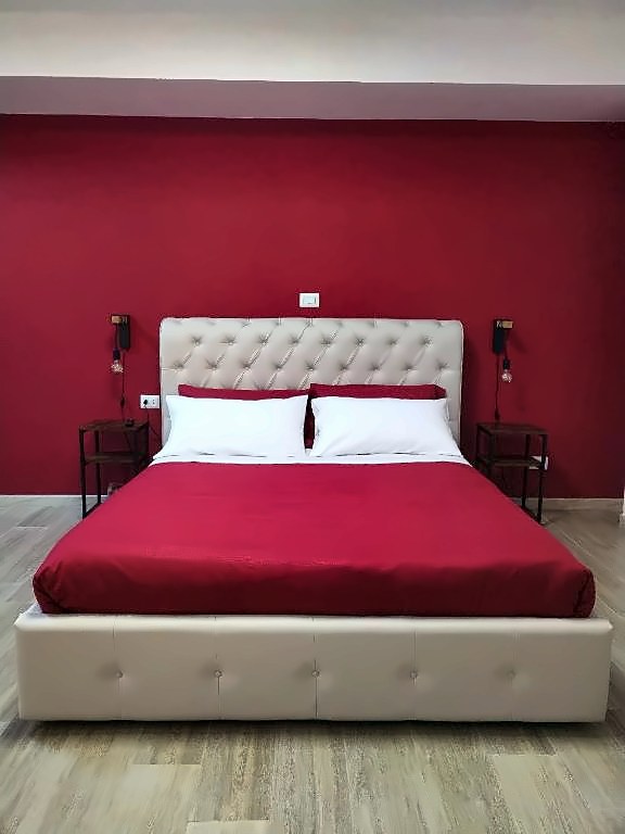 Letto matrimoniale con testiera imbottita davanti alla parete bordeaux